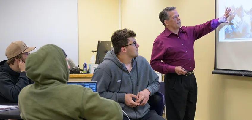 A teacher gestures toward a projected image during a business class